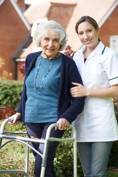 Cuidador ayudando a la mujer mayor a caminar en el jardín usando el marco que camina —  Fotos de Stock