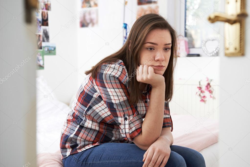 Depressed Teenage Girl Sitting In Bedroom