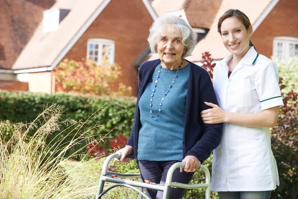 介護歩行車を使用して庭を散歩する年配の女性を支援 — ストック写真