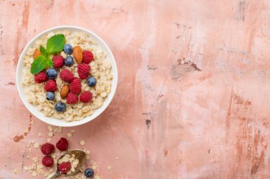 Ahududu, badem ve yaban mersinli yulaf ezmesi ve pembe arka planda nane.