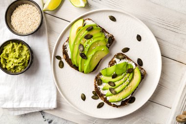 Beyaz tepsinin üstünde tahıllı ekmeğin üstünde krem peynirli avokado.