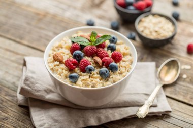 Ahududu, badem ve yaban mersinli yulaf ezmesi ve eski ahşap arka planda nane.