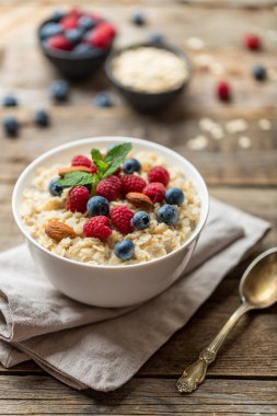 Ahududu, badem ve yaban mersinli yulaf ezmesi ve eski ahşap arka planda nane.