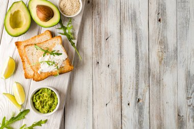 Avokado, krem peynir, limon, guacamole ve roka ile ahşap masada beyaz ahşap tepsi manzaralı tost. Metnin için alanı kopyala. Tarif.