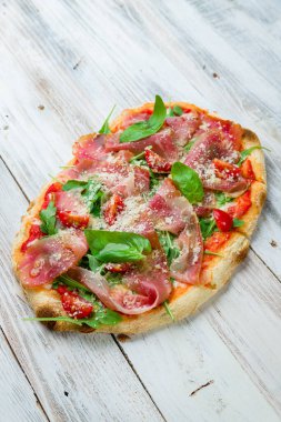 Beyaz ahşap tahtada parmalı jambonlu pizza.