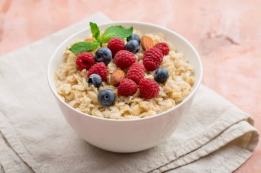 Ahududu, badem ve yaban mersinli yulaf ezmesi ve pembe arka planda nane.