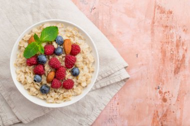 Ahududu, badem ve yaban mersinli yulaf ezmesi ve pembe arka planda nane.