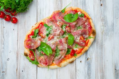 Beyaz ahşap tahtada parmalı jambonlu pizza.