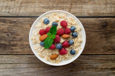 Ahududu, badem ve yaban mersinli yulaf ezmesi ve eski ahşap arka planda nane.