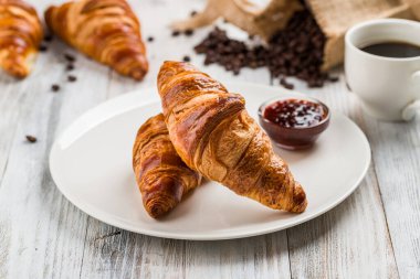 Beyaz plakalı klasik kruvasanlar. Hafif ahşap arka planda reçel var.