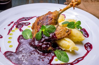 Kızarmış lezzetli ördek bacağı. Tabakta patates ve fesleğen yaprağı var. 