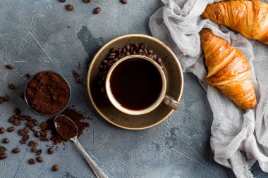 Kahve tozu ve kruvasanla gri taş masada bir fincan kahve.