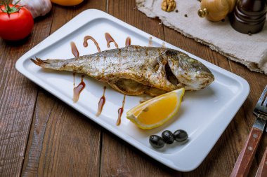 Dorado ızgarada, beyaz tabakta, tahta masada.