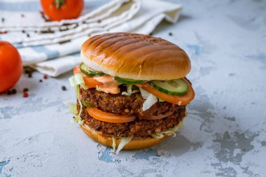 Falafel köfteli çift vejetaryen burger ve gri beton masada sebzeler.