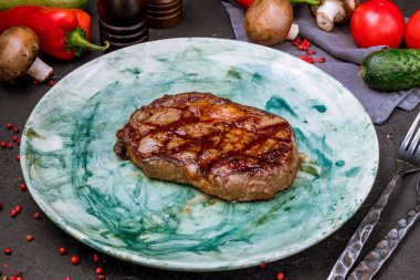 Sulu, yeşil tabakta, siyah beton masada biftek.