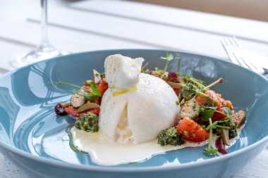 Ahşap masada mavi tabakta buratta peynirli salata.