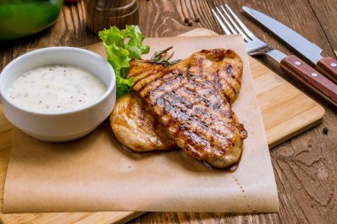 Ahşap masa arkasında ızgara tavuk göğsü.