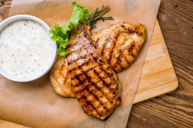 Ahşap masa arkasında ızgara tavuk göğsü.