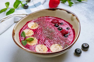 Meyveli smoothie kasesi ve gri arka planda muz.