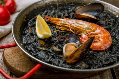 Ahşap zemin üzerinde deniz ürünleri olan siyah paella.