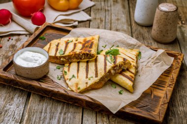 Eski ahşap masanın üstünde biftek ve soslu Quesadilla.