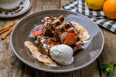 Tabakta Belçika waffle 'ı, dondurma, böğürtlen ve muz, ahşap arka planda.