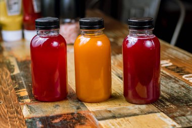 Ahşap masa arkasında yemek sosu olan üç küçük plastik şişe.  