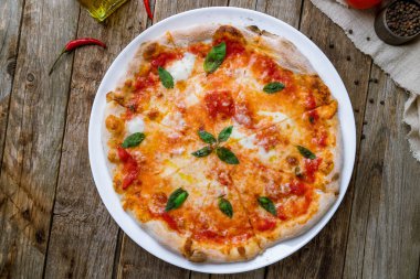 İtalyan pizzası Margherita, ahşap arka planda beyaz tabakta basil. 
