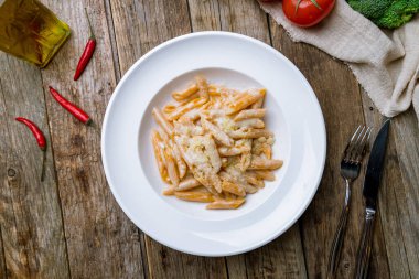 Penne dört peynir beyaz tabak üzerinde ahşap masa