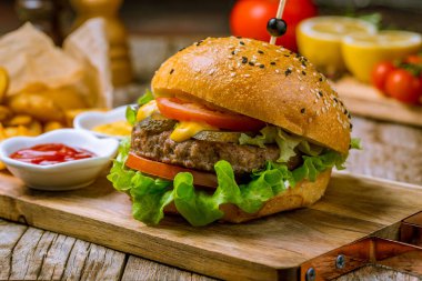 Tahtadaki ahşap masada etli peynirli ve sebzeli hamburger.