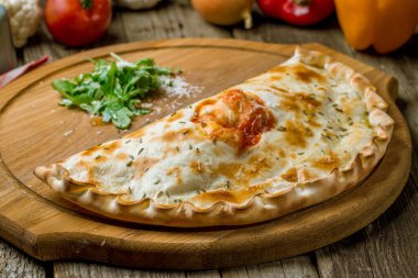 delicious closed calzone pizza on wooden board clipart