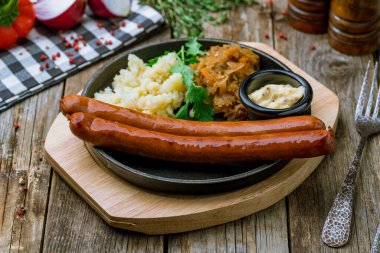 Fried bavarian hunter sausage with mashed potatoes, fried cabbage and sause on wooden background