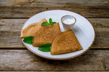 Eski ahşap masadaki beyaz tabakta ekşi kremalı krep.