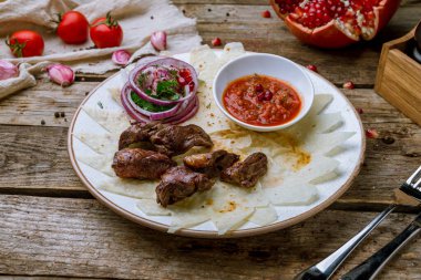 Kırmızı soğanlı kuzu kalbi ve ahşap masada domates sosu.