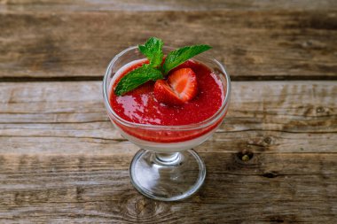 Çilek soslu panna cotta ve eski ahşap masada nane.