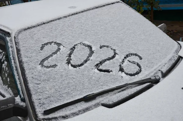 Kışın kar kaplı bir arabanın camına elle yazılmış 2026 numara. Kış mevsimi ve ulaşım