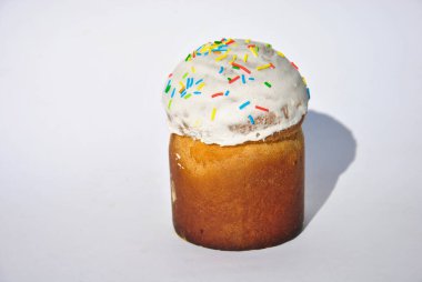 Beyaz şeker jöleli taze pişmiş Paskalya pastası ve parlak beyaz arka planda renkli serpiştirmeler. Yakın çekim, iştah açıcı doku, geleneksel Ortodoks Paskalya ekmeği, şenlik havası..