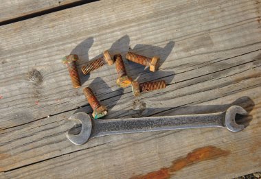 Eski ingiliz anahtarı ve paslı cıvatalar koyu ahşap arka planda.