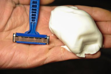El yapımı jilet ve bir tutam tıraş köpüğü tutan bir elin yakın çekimi. Erkek bakımı ve cilt bakımı konsepti.