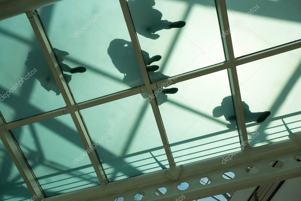 View from underneath at shadow of people walking on a semi-transparent glass bottom walkway in Vasco da Gama shopping mall, Lisbon, Portugal