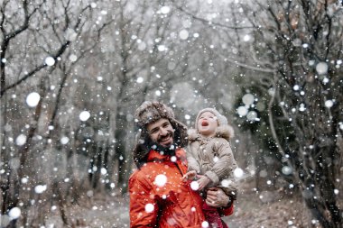 Sevgi dolu bir aile! Babası ve bebeği dışarıda oynuyorlar ve sarılıyorlar. Karlı kış yürüyüşüne çıkmış küçük bir çocuk ve baba. Uzun zamandır beklenen ilk kar yağışının konsepti