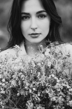 Uzun gömlekli çekici bir kadın otların ve kır çiçeklerinin arasında fotoğraf çektirmek için poz veriyor.