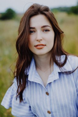 Uzun gömlekli çekici bir kadın otların ve kır çiçeklerinin arasında fotoğraf çektirmek için poz veriyor.