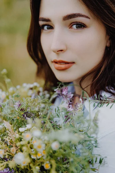 attractive woman dressed in a long shirt posing for a photo in a field among weeds and wildflowers