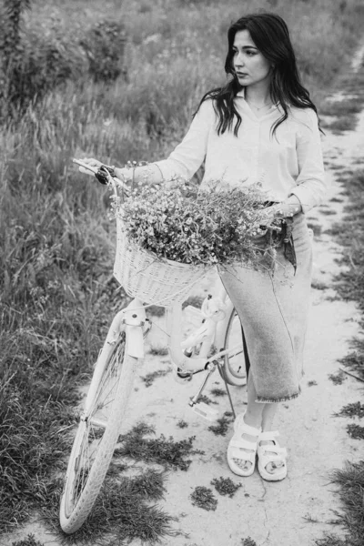 attractive woman dressed in a long shirt posing for a photo in a field among weeds and wildflowers
