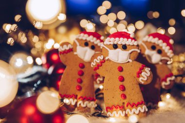 Yüzlerine tıbbi koruyucu maske takan zencefilli çöreklerle dolu bir Noel arkaplanı. Bir koronavirüs salgını sırasında 2021 yılını evde kutlama konsepti. Boşluğu kopyala