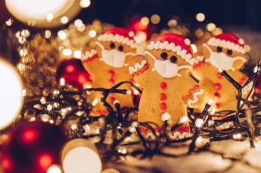 Yüzlerine tıbbi koruyucu maske takan zencefilli çöreklerle dolu bir Noel arkaplanı. Bir koronavirüs salgını sırasında 2021 yılını evde kutlama konsepti. Boşluğu kopyala