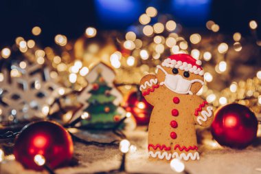 Yüzlerine tıbbi koruyucu maske takan zencefilli çöreklerle dolu bir Noel arkaplanı. Bir koronavirüs salgını sırasında 2021 yılını evde kutlama konsepti. Boşluğu kopyala