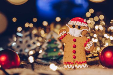 Yüzlerine tıbbi koruyucu maske takan zencefilli çöreklerle dolu bir Noel arkaplanı. Bir koronavirüs salgını sırasında 2021 yılını evde kutlama konsepti. Boşluğu kopyala