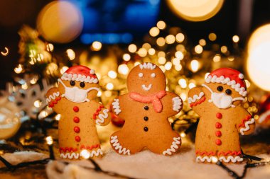 Yılbaşı ve Noel için ikramlar: Tıbbi solunum bandajı yüzü, cerrahi koruyucu maske, ışıklandırmalı parlak Noel arka planı ve Noel süslemeleri